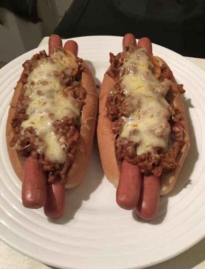 Two chili cheese hot dogs on a white plate, featuring melted cheese and ground meat toppings in hot dog buns.