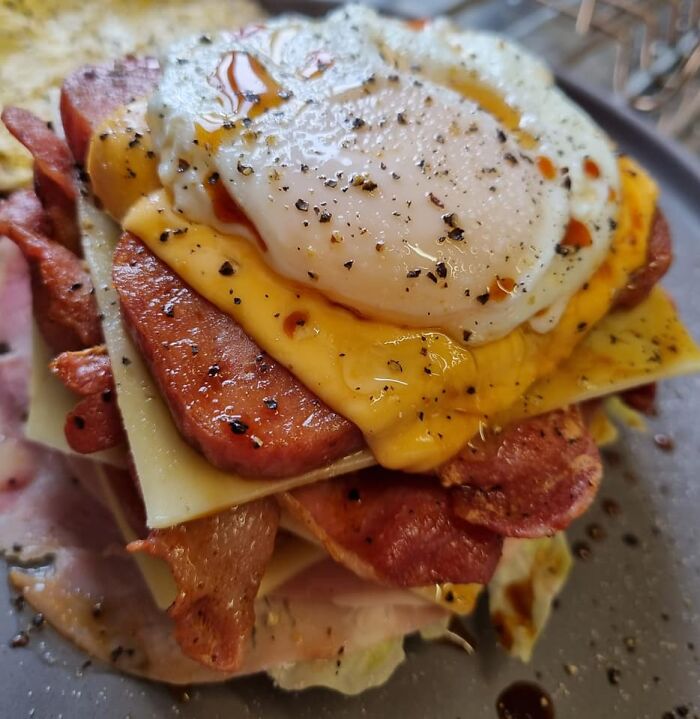 Close-up of a breakfast dish with fried egg, cheese, bacon, and sausage, featured in Facebook group rating dishes.