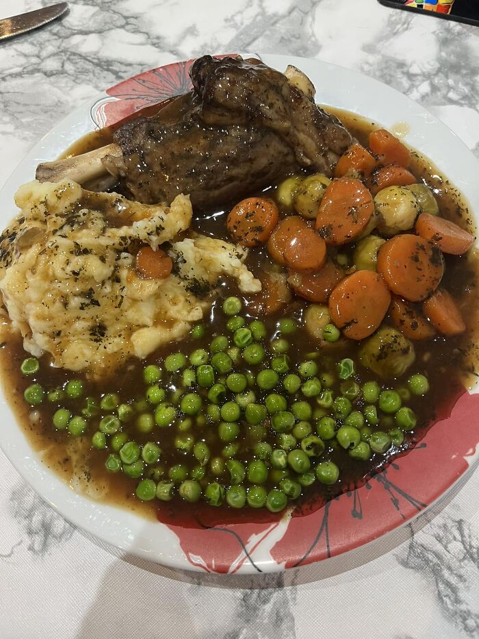 Hearty dish with lamb shank, mashed potatoes, carrots, peas, and gravy featured in a dish rating Facebook group post.