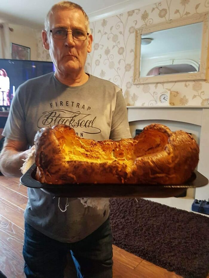 Man holding a large homemade dish in a kitchen, featured in a Facebook group where people rate others dishes.