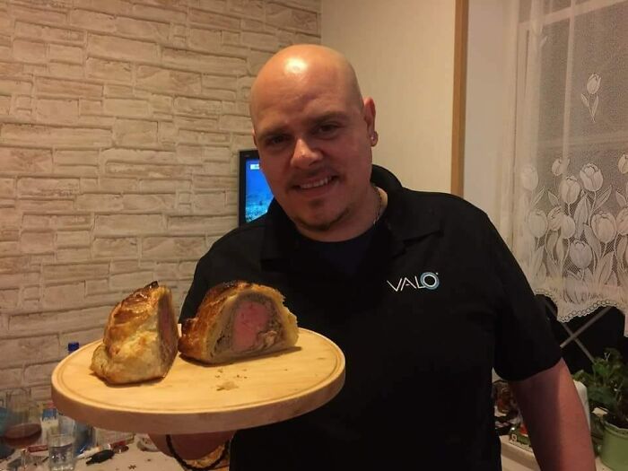Man holding a wooden board with a sliced beef Wellington as part of food dish ratings in a Facebook group.