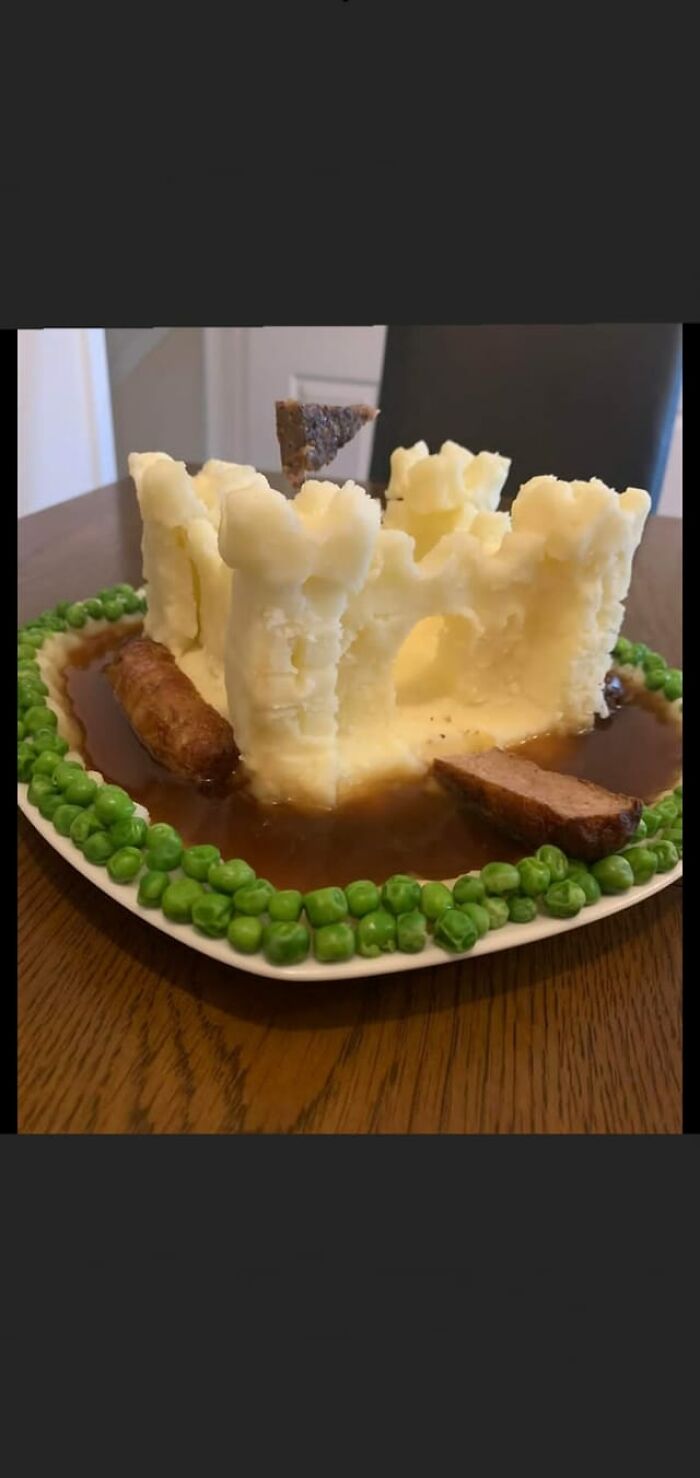 Mashed potato castle with gravy moat, sausages, and peas on a plate from a dish rating Facebook group.