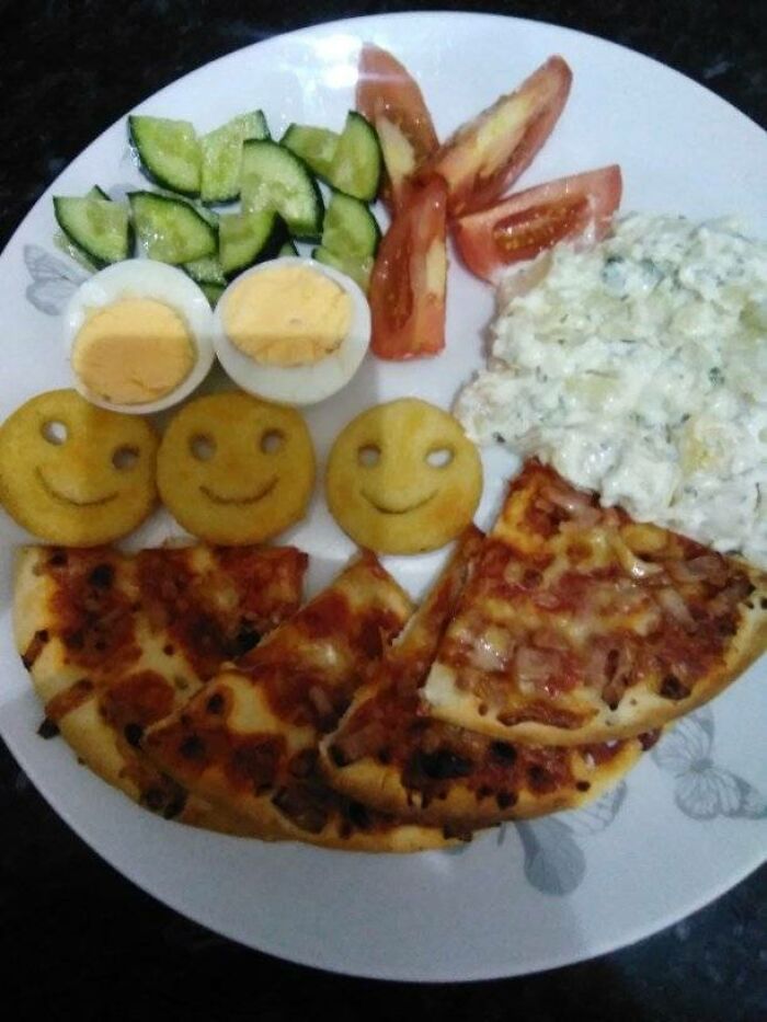 Plate of rated dishes featuring pizza slices, smiley face potatoes, sliced cucumber, boiled eggs, tomato wedges, and creamy salad.