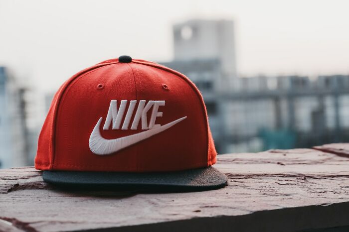 Red Nike cap with white logo placed on a ledge featuring urban buildings in the blurred background.