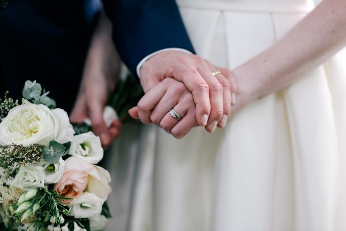 Close-up of a couple holding hands with wedding rings and a bouquet, symbolizing support and facing fears together.