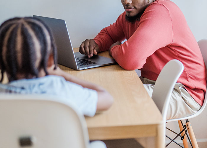 Man sharing annoying experiences related to his gender while sitting at a table with a child using a laptop nearby.