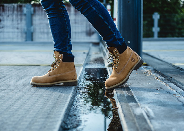 Man in brown boots stepping over a puddle on the street, illustrating common challenges men experience because of their gender.