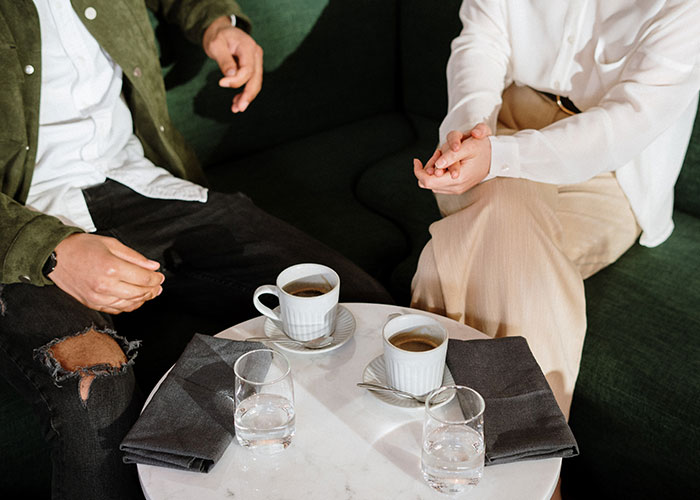Two people sitting on a green couch having coffee and water, discussing annoying things men experience because of their gender.