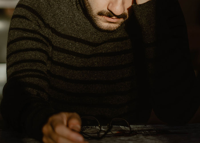Man in striped sweater looking down, appearing frustrated and reflective, highlighting annoying experiences men face.