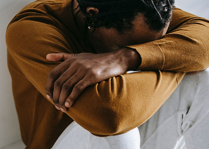 Man in a brown sweater sitting with head on arms, expressing frustration with annoying things men experience because of their gender