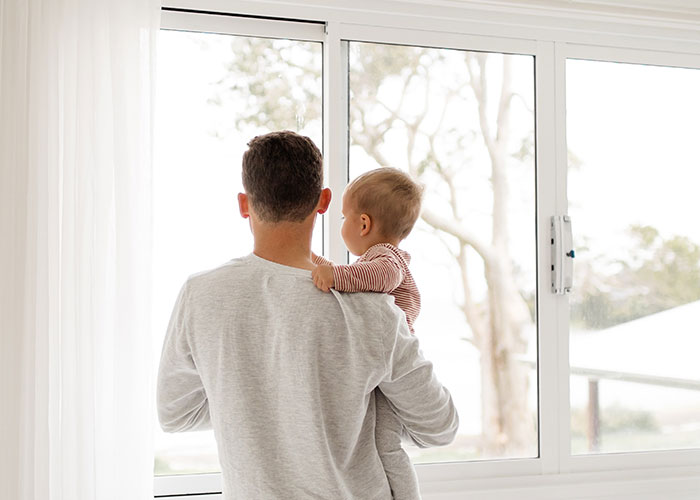 Man holding baby by the window, illustrating common annoying things men experience because of their gender.
