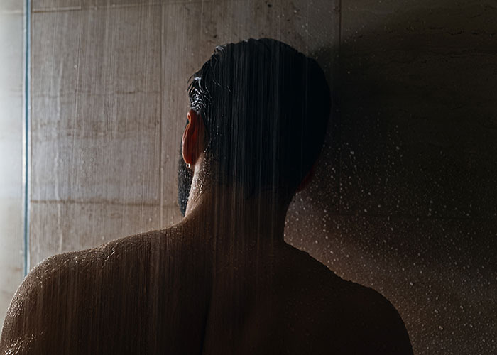 Man with wet hair standing under a shower, illustrating common annoying experiences men face due to their gender.