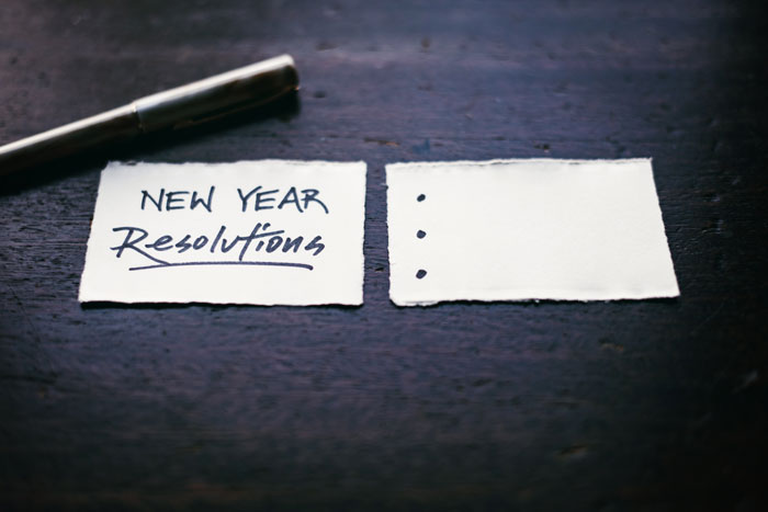 New Year's resolutions written on paper with pen on a dark wooden table.