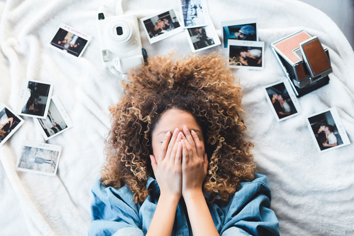 Woman enjoying New Year’s Eve, surrounded by polaroid photos and a camera, hands covering face playfully.