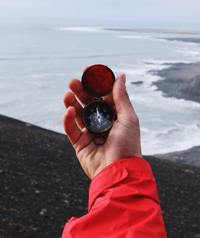 Person holding a compass near the ocean, exploring cool things to do on New Year’s Eve.