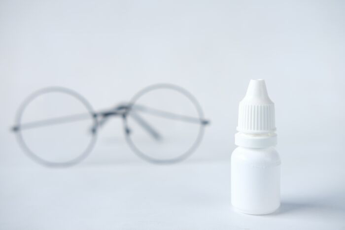 A small white bottle in focus with blurred round eyeglasses in the background, illustrating fear of going downstairs after lights off.