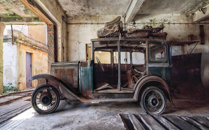 Abandoned factory interior with a rusty classic car covered in dust and debris, showcasing unexpected vintage vehicle finds.