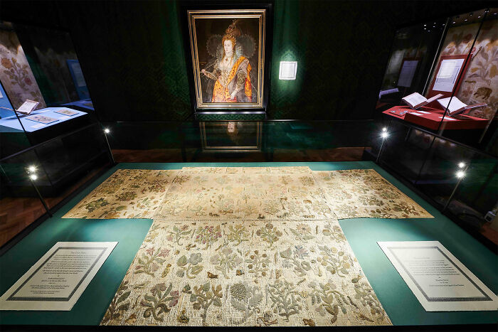 Exhibit of vintage embroidered clothing with a historical portrait in the background, showcasing weird history facts.