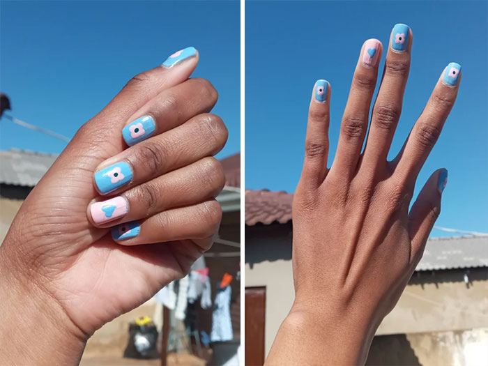 Close-up of hands featuring blue and pink nail art designs with tiny floral and heart patterns under a clear sky.