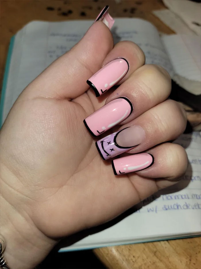 Hand with pink and lavender nail art featuring black outlines and minimalist designs, showcasing creative nail art ideas.
