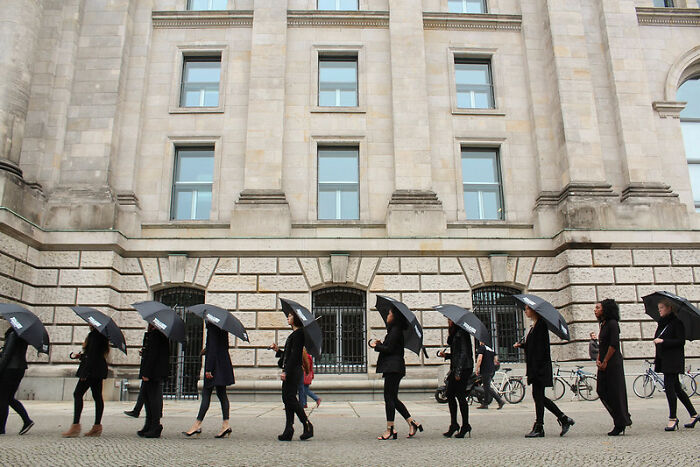 People walking in a line holding black umbrellas, symbolizing the road to hell paved with good intentions concept.