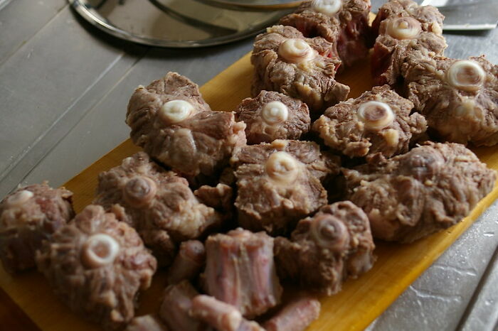 Close-up of chopped oxtail pieces on a wooden board, representing peasant food now hard to afford.