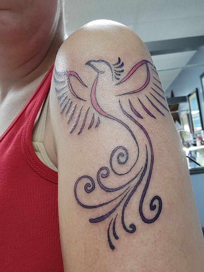 Phoenix tattoo on a person's upper arm with elegant, swirling lines in black and pink, wearing a red tank top.