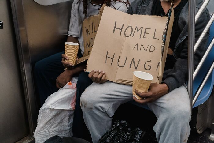 Two people holding cardboard signs about homelessness and hunger, highlighting alarming number of individuals not knowing basic facts.
