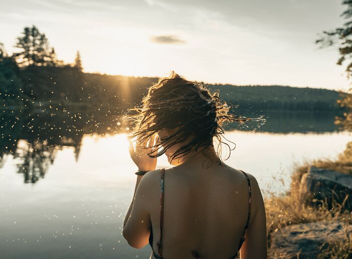 Person by a lake at sunset, hair blowing in the wind, reflecting on basic facts many people do not know.