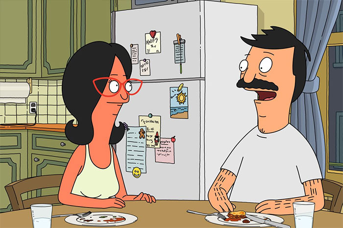 Cartoon couple enjoying breakfast at the kitchen table with a fridge in the background.