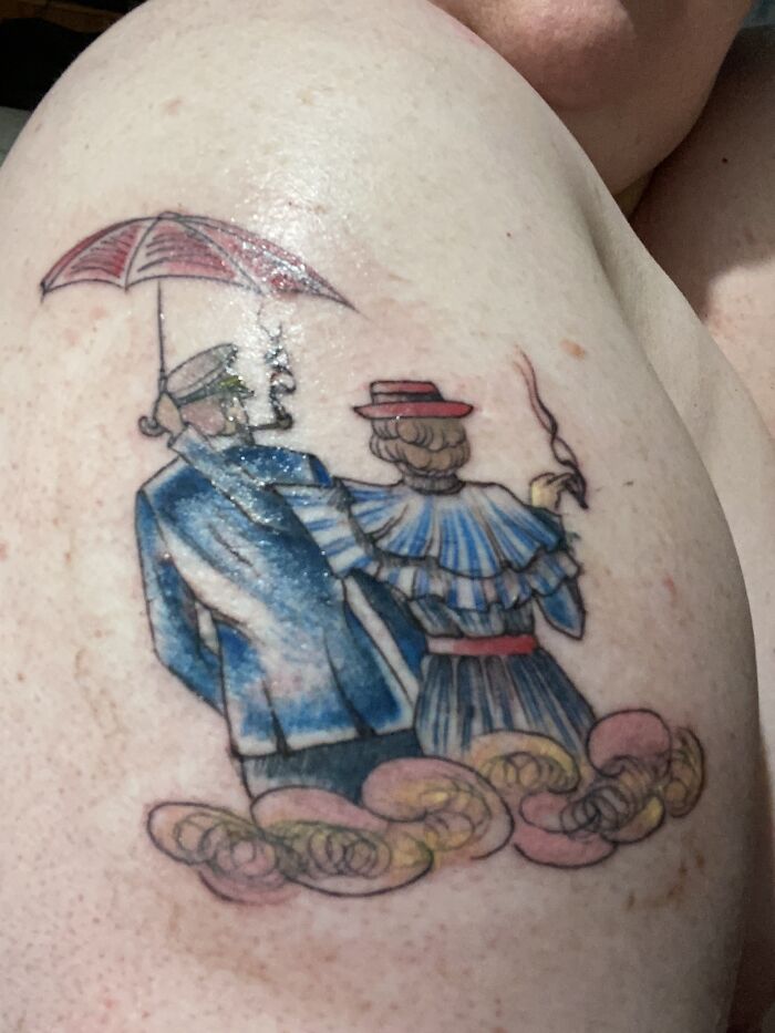 Tattoo depicting two figures with an umbrella, in vintage attire, on skin.