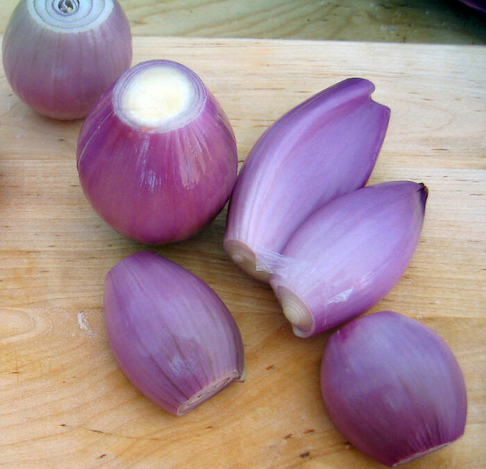 Purple shallots peeled and sliced on a wooden cutting board, illustrating a once affordable peasant food product.