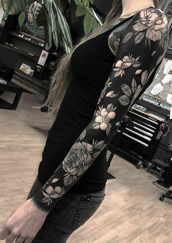 A person with a beautifully executed black and white floral sleeve tattoo, standing in a tattoo studio.