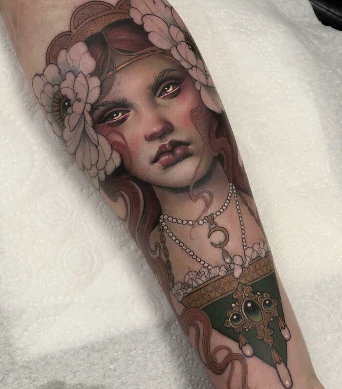 Beautiful tattoo idea of a woman's face adorned with flowers and jewelry, executed perfectly on forearm.