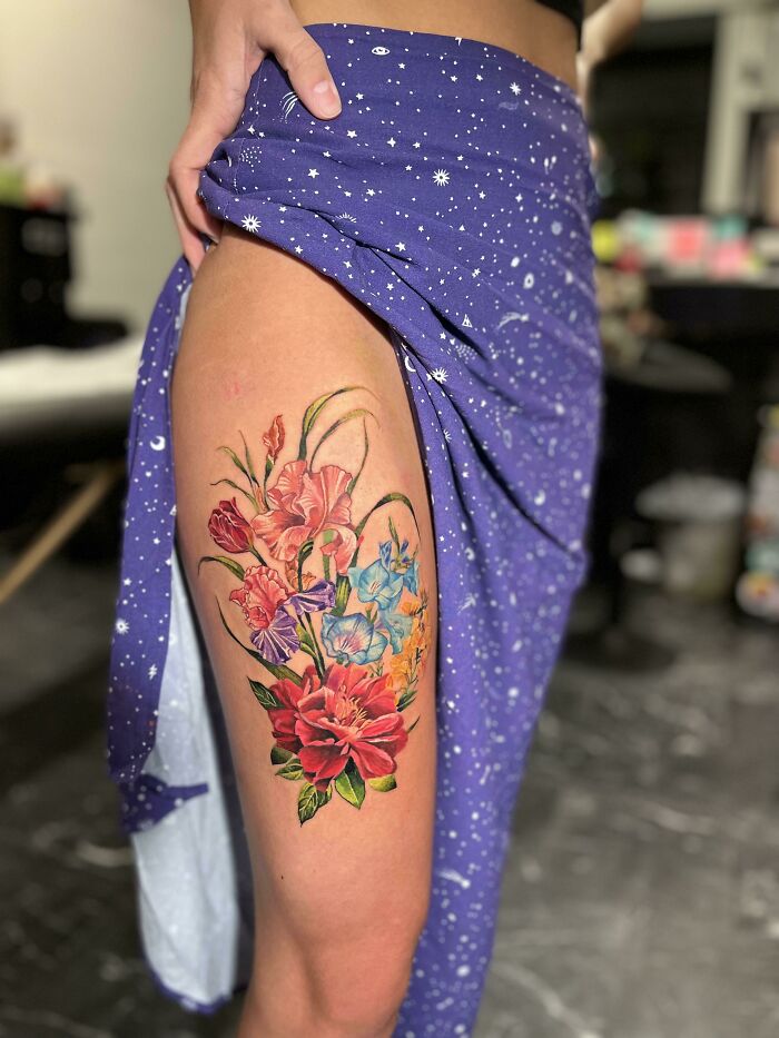 Beautifully executed floral tattoo on a person's thigh, showcasing vibrant colors and detailed artistry.