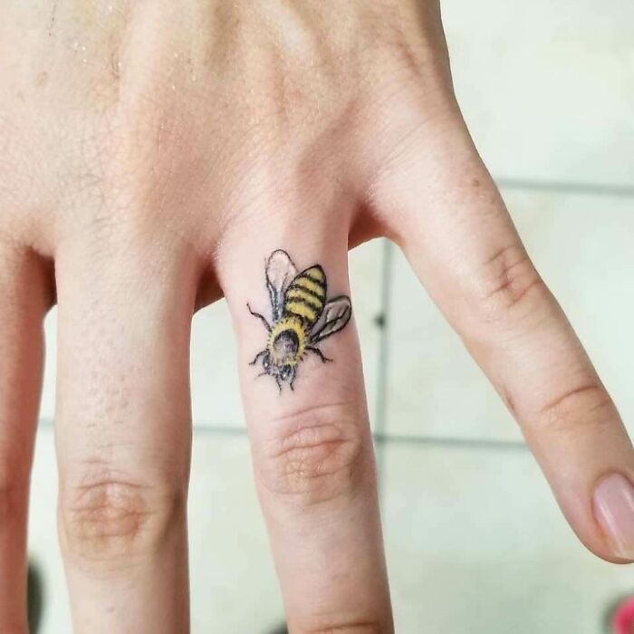 A delicate bee tattoo executed perfectly on a finger.