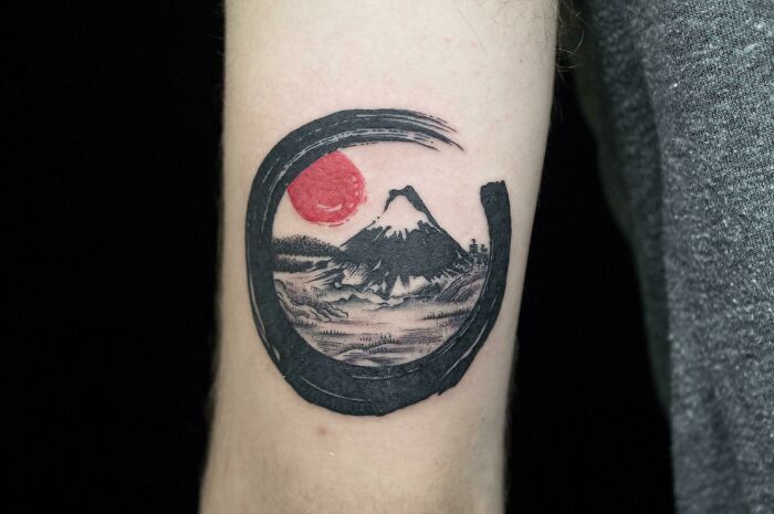 Beautiful tattoo idea of a landscape with a mountain and red sun, executed perfectly on an arm.