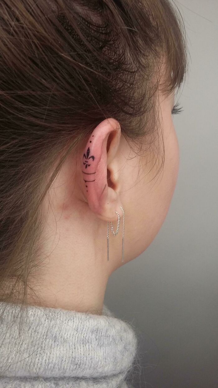 Ear tattoo with fleur-de-lis design executed perfectly, paired with elegant chain earrings.