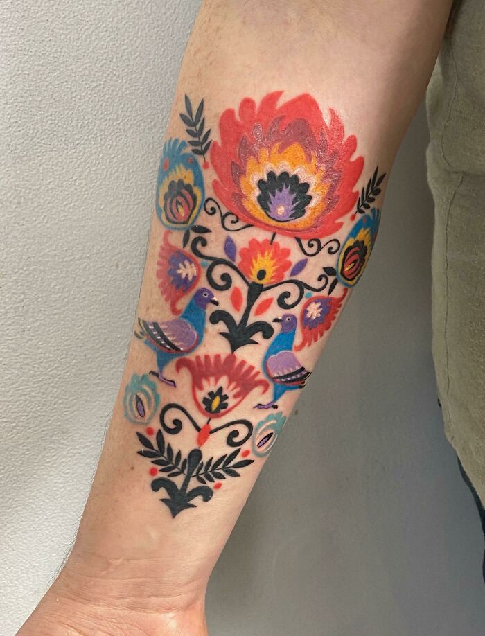 Colorful floral tattoo on forearm, beautifully executed with vibrant flowers and birds.