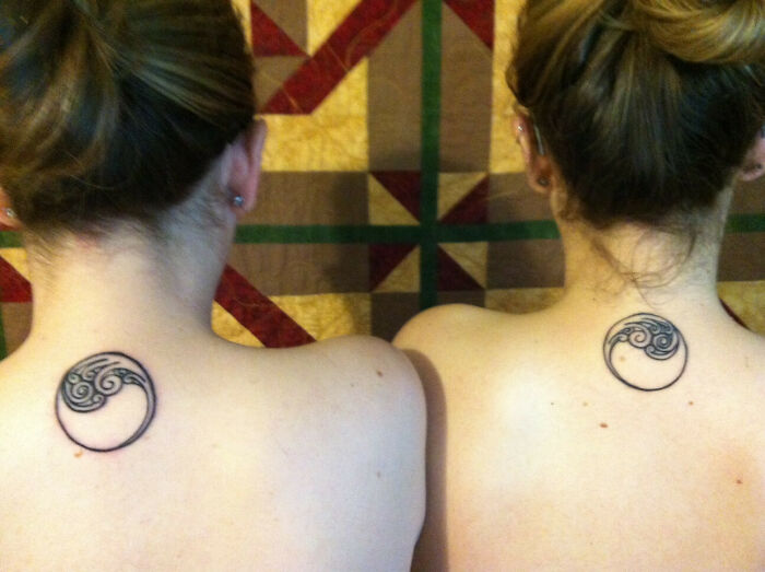 Two people with matching brother and sister tattoos on their upper backs, featuring a yin-yang design.