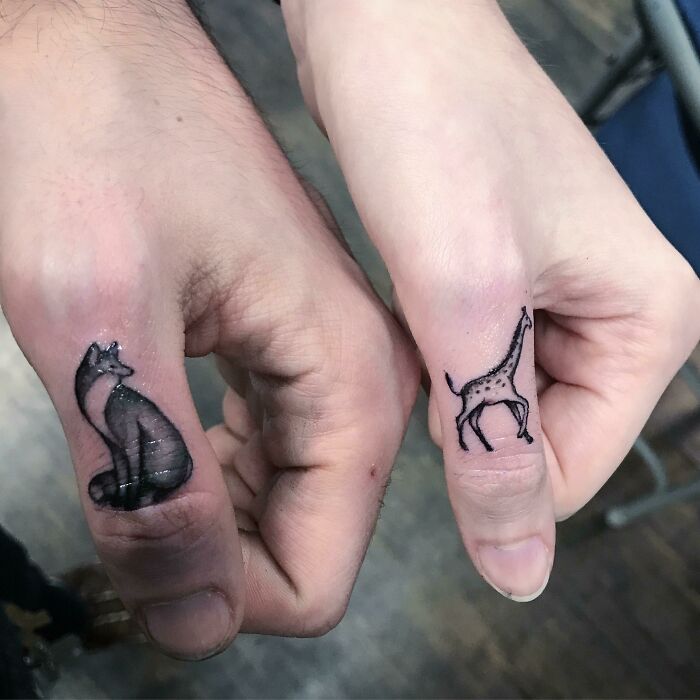 Brother and sister tattoos featuring a fox and a giraffe on two thumbs.