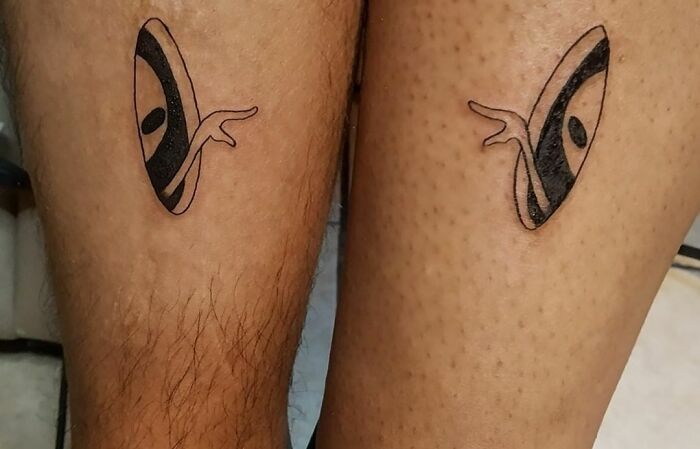 Small, simple brother and sister tattoos with abstract eye design on legs.