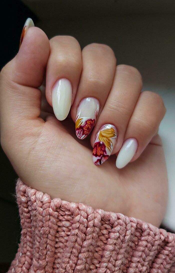 Hand with almond-shaped nails featuring floral nail art ideas in shades of red and yellow on a neutral background.