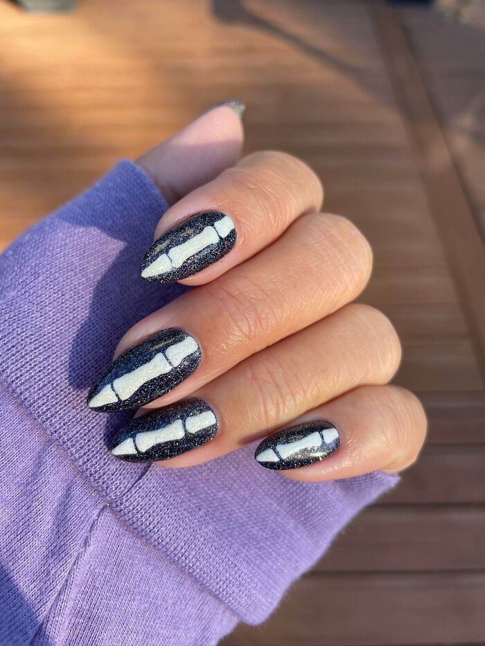 Black glitter nails with white bone nail art design on almond-shaped nails, showcasing creative nail art ideas.