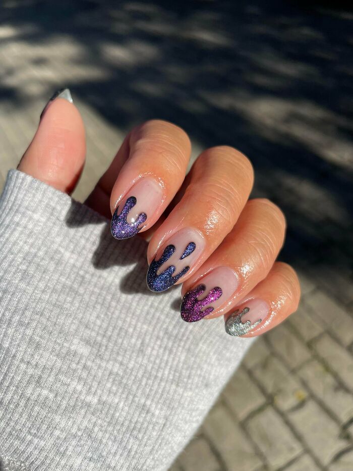 Close-up of hand with glittery drip nail art designs in purple, blue, and silver, showcasing creative nail art ideas.
