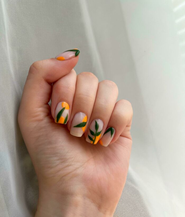 Hand with nail art featuring green leaves and orange shapes on a neutral background, showcasing creative nail art ideas.