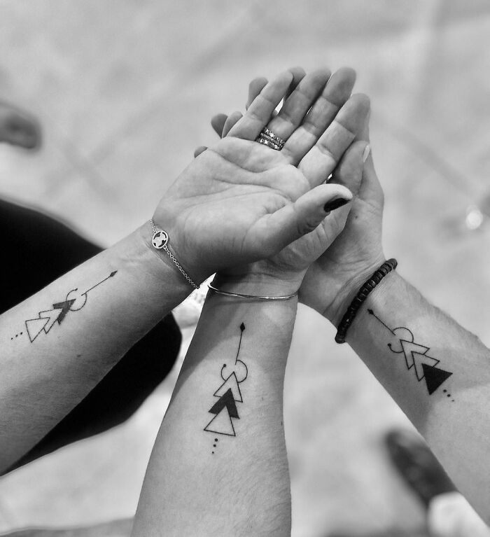 Three arms with matching small, simple brother and sister tattoos featuring geometric arrows.