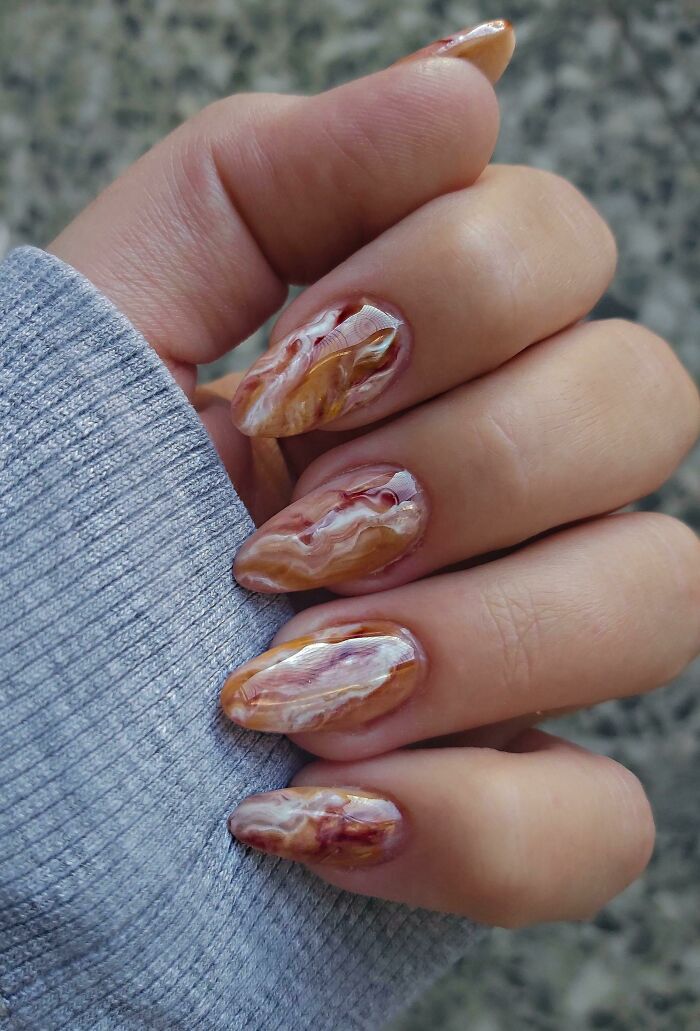 Close-up of a hand with marble-inspired nail art design, featuring swirls of gold, brown, and white.