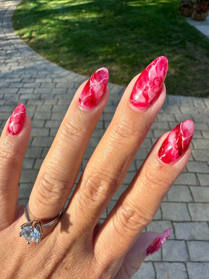 Close-up of hand with red and white marble nail art designs, showcasing creative nail art ideas on long nails outdoors.