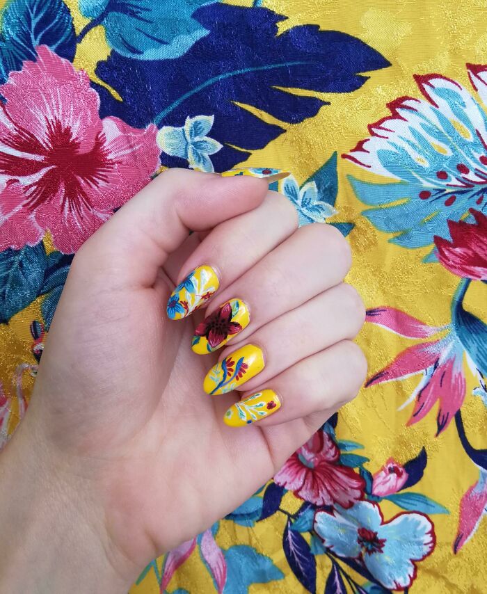 Hand with yellow floral nail art designs matching a colorful tropical floral fabric background, showcasing creative nail art ideas.